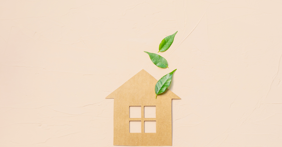 A cut-out house with green leaves rising from its chimney, symbolising eco-friendly living and sustainability, placed on a beige background.