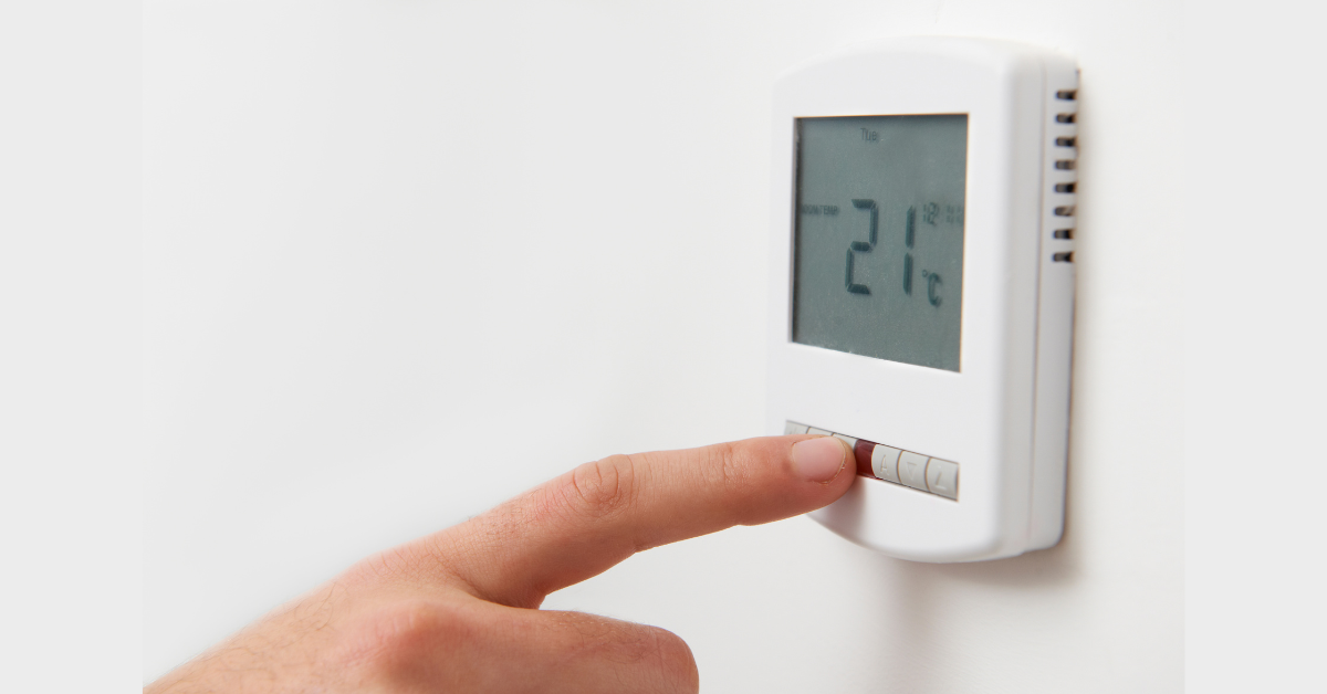 A hand adjusting the temperature on a digital wall-mounted , illustrating the importance of optimising thermostat use for energy efficiency and comfort